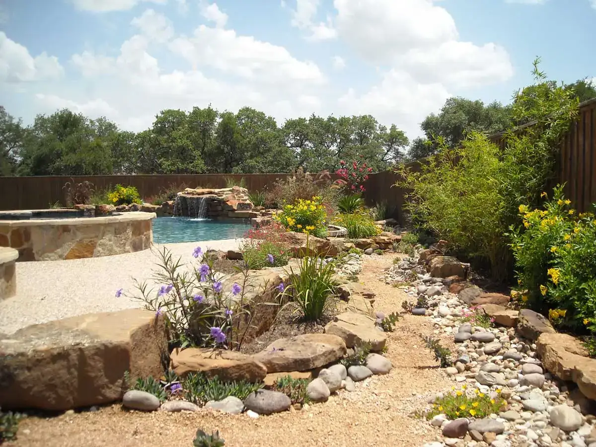 Xeriscape pool with stone hardscapes, waterfall feature, and drought-tolerant plants in a natural setting