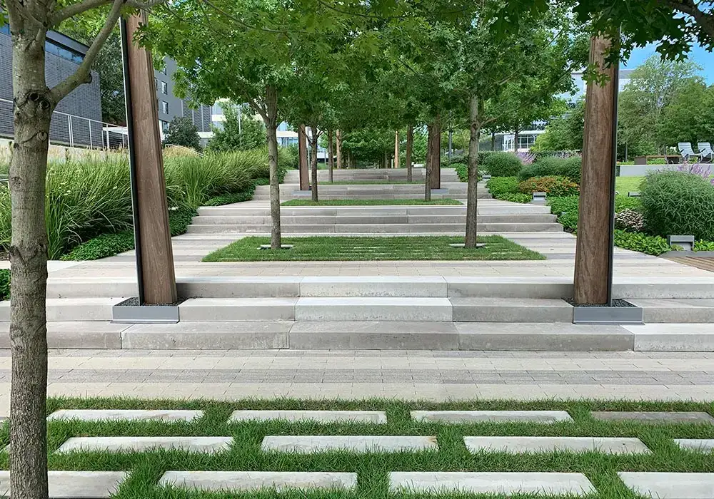 Modern hardscape design featuring concrete steps, grassy sections, and wooden pillars, surrounded by lush greenery