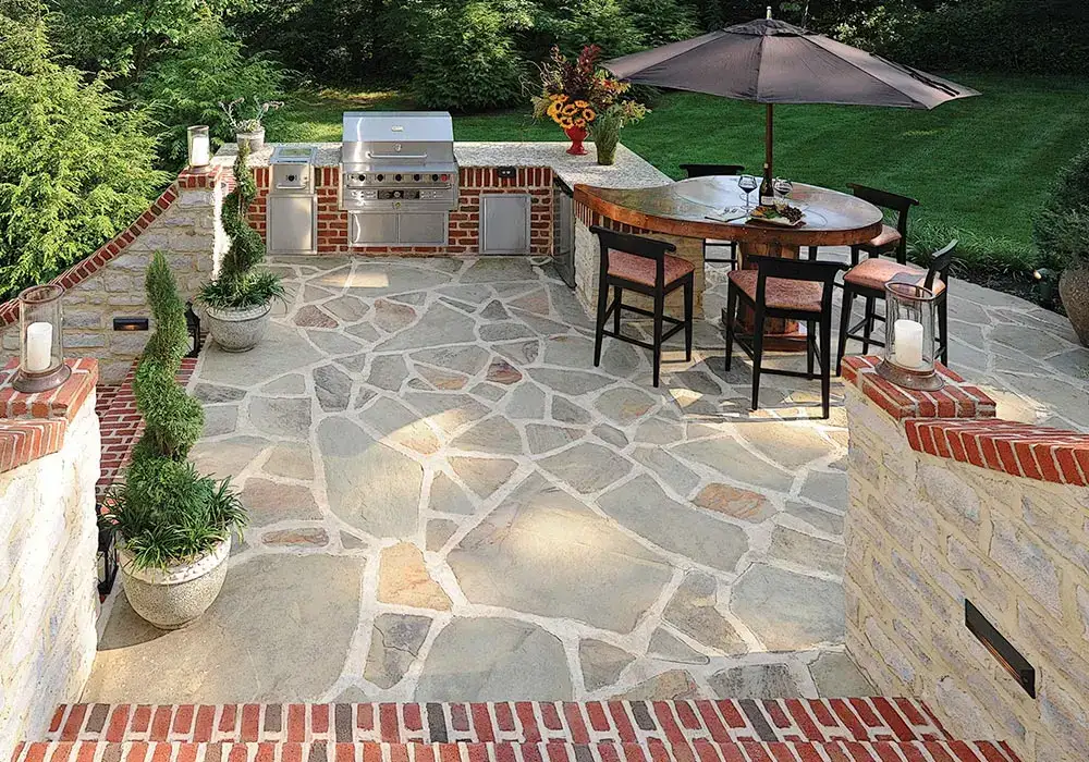 Outdoor kitchens with a built-in grill, brick accents, and a flagstone patio, featuring a dining area with umbrella seating