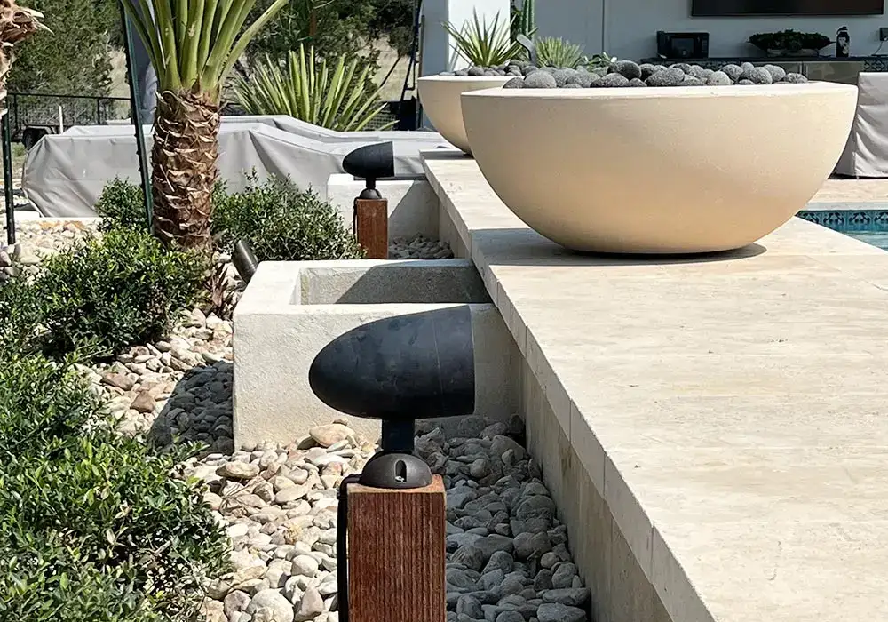 Modern hardscapes featuring a sleek stone planter, landscape lighting, and a pebble bed surrounding greenery