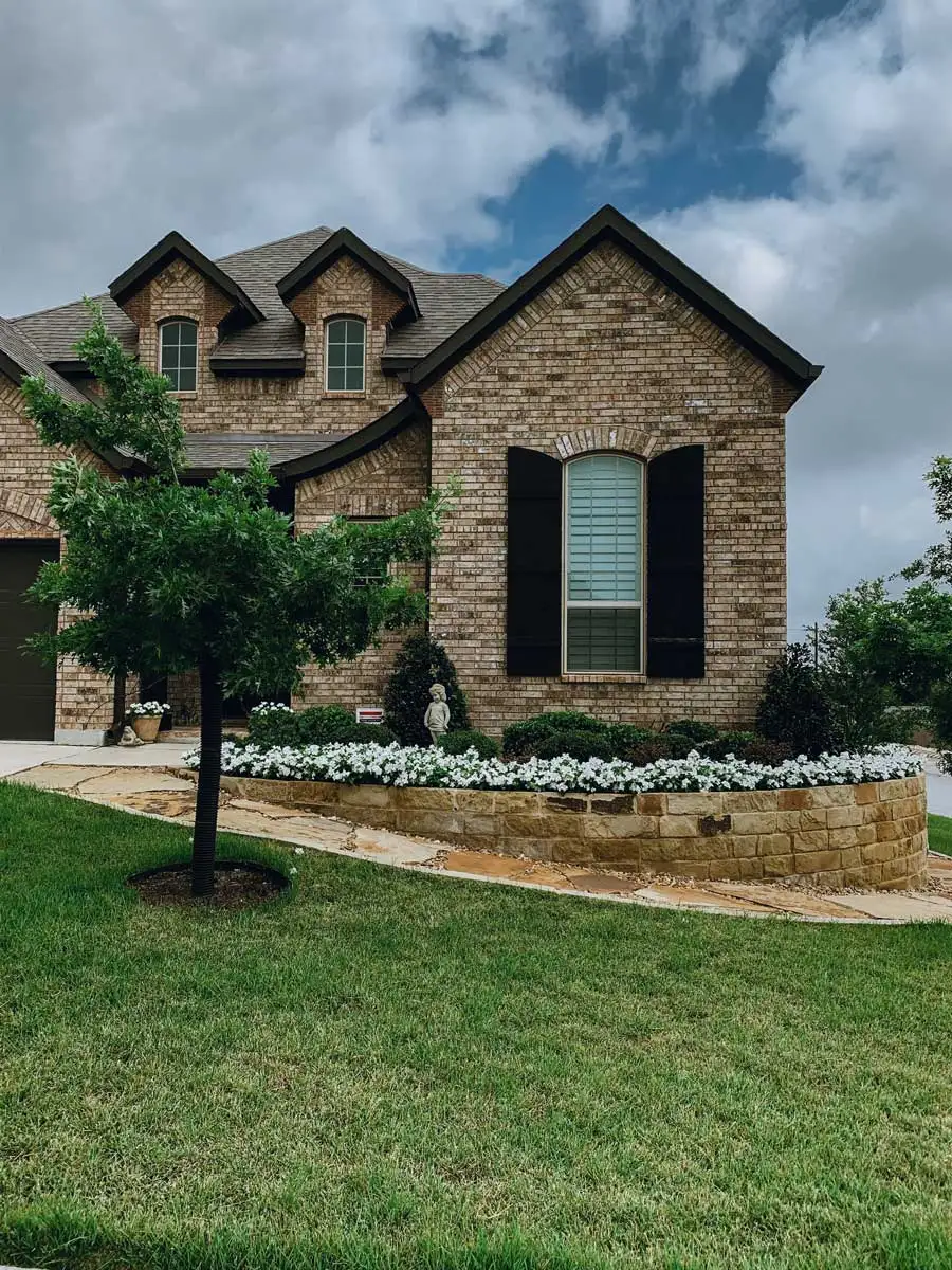 Brick home with a curved stone retaining wall, manicured lawn, and flower bed, blending hardscapes with softscapes